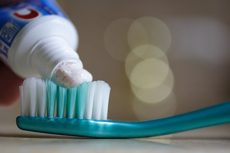 tooth paste being squeezed out onto a tooth brush. the tooth paste has red microbeads in the white paste.